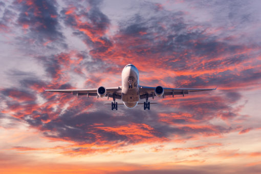 Landing airplane. Landscape with passenger airplane is flying in the blue sky with red, purple and orange clouds at sunset.